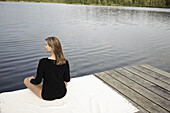 Young woman sitting on jetty at lake Starnberg, Bavaria, Germany