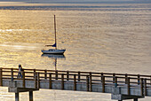 Sailboat anchored in Bellingham Bay with the boardwalk of Boulevard Park in the foreground,  the San Juan Islands are in the distance,  Bellingham Washington USA