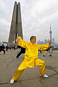 Chinese man practicing tai chi in the early morning in Huangpu Park with the Monument to the People´s Heroes in the background,  Shanghai,  China