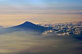 A volcanic mountain peak rising above the clouds in early morning light