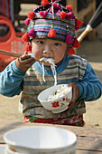 Hmong boy stuffing his face with noodles at market in Tam Duong near Sapa Vietnam