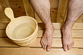 Wooden bucket and legs of a man sitting in sauna