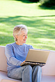 Absorbed, Adult, Adults, Calm, Calmness, Caucasian, Caucasians, Color, Colour, Computer, Computers, Contemporary, Couch, Couches, Daytime, exterior, Female, Garden, Gardens, Gray-haired, Grey hair, Grey haired, Grey hairs, Grey-haired, grin, grinning, Hob