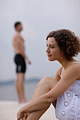 Woman sitting on jetty, man in background, Starnberger See, Upper Bavaria, Germany