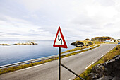 Kurvenreiche Küstenstraße mit Warnschild, Lofoten, Norwegen, Skandinavien; Verkehrschild, Europa
