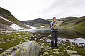 Young woman looking at map of trails in a rocky landscape at the Rimstigen, Naerofjord, Sogn og Fjordane, Norway, Scandinavia, Europe