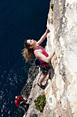 Eine junge Frau, und ein junger Mann klettern an den Klippen der Bucht von Zurrieq, Malta, Europa