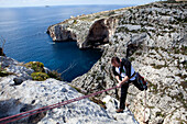 Ein Mann seilt in die Bucht von Zurrieq ab, im Hintergrund die Blue Grotto, Malta, Europa