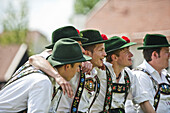 Young men wearing traditional costumes sitting side by side, May Running, Antdorf, Upper Bavaria, Germany
