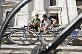 Junges Paar mit Fahrrädern rastet auf den Stufen vor einem Haus, Urbino, Marken, Italien, Europa