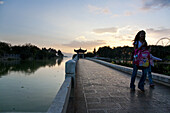 Mother and daughter on a bridge at Dianchi Lake at sunset, Daguan Park, ferris wheel and pavillion in the background, north-west of Kunming City, Kunming, Yunnan, People's Republic of China, Asia