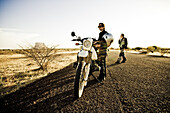 Woman and man with motorcycles on a road in the evening sun, Hombori, Mali, Africa