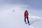 Frau auf Skitour steigt mit Ski auf, Felsen im Nebel im Hintergrund, Schusterkogel, Saalbach-Hinterglemm, Kitzbüheler Alpen, Salzburg, Österreich