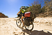 Frau fährt mit Mountainbike auf einer Sandpiste, Madagaskar