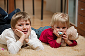 Junge (6 Jahre) und Mädchen (2 Jahre) liegen auf einem Teppich