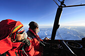Zwei Personen in Heißluftballon blicken auf verschneite Alpen, Luftaufnahme, Tirol, Österreich, Europa