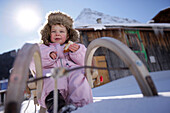 Kleinkind auf einem Schlitten vor einer Hütte, Galtür, Paznauntal, Tirol, Österreich