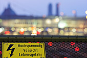 High voltage sign, Munich main station and the twin towers of the Frauenkirche cathedral out of focus in the background, Munich, Upper Bavaria, Bavaria, Germany