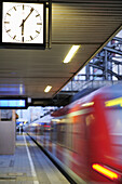Platform with clock, suburban train in motion out of focus in the background, Munich, Upper Bavaria, Bavaria, Germany