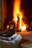 Zwei Personen wärmen sich die Füße vor einem Kaminfeuer