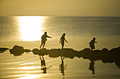 Silhouettes of children playing on a stonewall in the sea