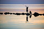 Silhouettes of children playing on a stonewall in the sea