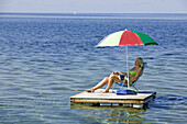 Woman on a raft sitting under a brightly-coloured umbrella