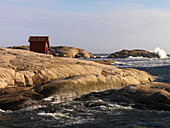 Woman sits by red hut on cliffs, Bohuslan, Sweden