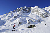 Female backcountry skier ascending to Hocharn, Hoher Sonnblick in background, Rauris valley, Goldberg mountain range, Hohe Tauern, Salzburg state, Austria