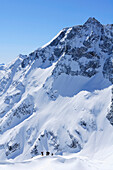 Gruppe von Skitourengehern tief unter Hoher Sonnblick mit Zittelhaus am Gipfel, Rauriser Tal, Goldberggruppe, Hohe Tauern, Salzburg, Österreich