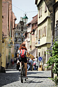 Female cyclist passing cobblestone, Roederbogen, Rothenburg ob der Tauber, Altmuehltal cycle trail, Bavaria, Germany