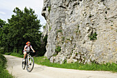 Female cyclist passing rock face, Altmuehltal cycle trail, Altmuehltal natural park, Altmuehltal, Bavaria, Germany