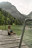 Young girl sitting on a wooden platform on lake Gleinkersee, Windischgarsten, Austria, Alps, Europe