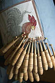 German Bobbin Lace (Kloppelei ) project: a rooster is designed in colored thread, each thread on its own bobbin