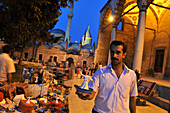 Verkaüfer zeigt eine kleine Derwischstatuette neben Yusufaga-Moschee u. Mevlana Takkesi, Konya, Anatolien, Türkei
