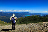 Woman looking from the mountain top of Monte Tamaro to Lugano and the Lago di Lugano, hike in the mountains to Monte Tamaro, Ticino, Switzerland
