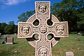 Cross headstone with faces on it at ´ Beechbrook Cemetery´ in Gloucester, Massachusetts USA , which is in an scenic New England graveyard