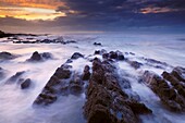 The incoming tide washing over the rocks at dusk at Westward Ho! in Devon, England