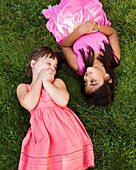 A little caucasian girl and an Asian Indian girl lay in the grass to relax and play