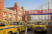 Yellow ambassador taxis outside Howrah train station with Howrah bridge in background, Kolkata, West Bengal, India