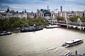 Aerial view of ships and boats on the Thames river with the Hungerford bridge on the background, London, England, United Kingdom Tilted lens used for shallow depth of field