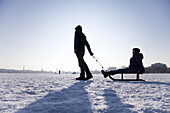Zwei Personen mit einem Schlitten auf zugefrorener Außenalster im Winter, Hamburg, Deutschland