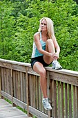 30 year old blonde woman in work out clothes looking away from camera while sitting on a railing