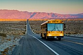 School bus on long straight two lane desert road at sunrise, Anza Borrego Desert State Park, San Diego County, California