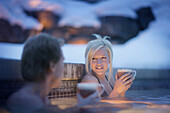 Woman and man with drinks bathing in outdoor pool, Four Seasons Resort Whistler, Whistler, British Columbia, Canada