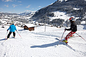 Children skiing on fresh primed ski piste, Schlosslelift, Hirschegg in background, Kleinwalsertal, Vorarlberg, Austria