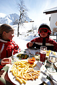 Ski fahrende Kinder bei Mittagspause auf einer Hotelterrasse, Hirschegg, Kleinwalsertal, Vorarlberg, Österreich