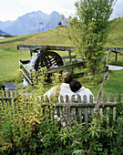 Paar sitzen auf einer Bank und schauen Richtung Wasserrad, Naturhotel Chesa Valisa, Hirschegg, Kleinwalsertal, Österreich