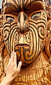 Maori carving, a tourist's hand feels texture of face, Rotorua, New Zealand