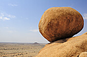 Red balancing granite rock on slab in front of savannah, Great Spitzkoppe, Namibia